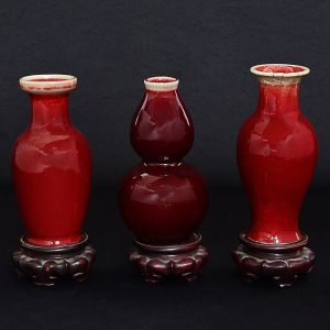 <b>Conjunto de 3 pequenos vasos </b>em porcelana chinesa cobertos por esmalte sangue de boi. Dois em forma de segmento de balaústre e um em forma de bulbo. Borda de um deles colada. Alt. 18 e 17 cm