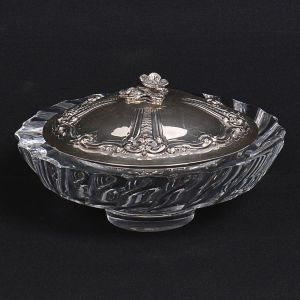 "<b>Bombonnière</b>" em grosso cristal lapidado em ondulações levemente torcidas. Tampa em prata brasileira decorada com flores e volutas com marca da Casa União. Borda do cristal com bicadinhos. Alt. 13 cm; Diâm. 22 cm