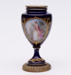 Ânfora em porcelana possivelmente austríaca, Velho Viena, na cor predominante azul cobalto e detalhe de figura de dama. Base em bronze. Pequeno lascado na base (vide foto). Altura: 20 cm