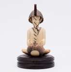 Escultura em marfim representando figura de tecelão apoiado em base de madeira. Altura total: 24 cm.