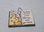 Placa decorativa na forma de livro, descrevendo idades da mulher em italiano, em cerâmica. Medindo 13,5cm x 10,5cm. Com restauro.