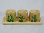 Três cachepot com bandeja, cerâmica esmaltada na cor bege, decorados com cactos em policromia. Med. do cachepot 7 x 7cm e da bandeja 27 x 10cm.