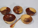 Cinco peças em madeira, sendo pote com tampa e colher e quatro bowls. Um dos bowls apresenta fissura na borda. Med. do bowl 5 x 14cm.