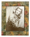 Quando decorativo contendo reprint de fotografia em sépia da atriz hollywoodiana Lauren Bacall, protegida por moldura fartamente decorada com motivo floral em policromia e vidro transparente. Mede 38cm x 46cm.