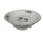 KPM - Krister Porzellan-Manufaktur, Waldenburg - Alemanha (Fundada em 1831 por Karl Kristen), Fruteira de pé confeccionada em porcelana polaca esmaltada na tonalidade branca, elementos vegetalistas em relevo, pintura de pássaro, flores e folhagens em policromia, borda e filetes em ouro, medindo 8,5x27cm.