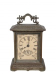 RELÓGIO, Relógio de mesa, cornija ou estante, modelo dito CARRIAGE, mecânico, a corda, mecanismo da manufatura ANSÔNIA CLOCK (fundada em Connecticut no ano de 1851, por Anson Green Phelps e mais dois relojoeiros Theodore Terry e Franklin C. Andrews, como subsidiária de sua empresa Ansônia Brass, fundada anteriormente em 1844 para fornecer laminados em latão para confecção de relógios, em 1877 adquiriram uma fábrica em New York e transferiram a maior parte de sua produção; em 1878 Thomas Edison visitou a fábrica para experimentar a combinação de relógios com o seu fonógrafo; em 1879 uma segunda fábrica foi aberta no Brooklyn; em 1880 a fábrica de New York incendiou; em 1881 foi reaberta após ter sido reconstruída no mesmo lugar; em 1883 fechou a fábrica de Connecticut; em 1929 foi vendida para Amtorg, que pertencia ao governo Soviético; em 1969 os direitos do uso do nome foram transferidos para Ansônia Clock Company, Lynnwood, Washington), mostrador com algarismos romanos, caixa com cinzelado de florões, aro frontal com mossa e vidro solto, não testado e sem garantia de funcionamento, medindo 19x12,5x8,5cm.