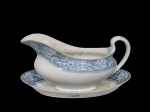 JOHNSON BROS (Staffordshire, Inglaterra, 1883), Molheira com presentoir confeccionada em faiança inglesa vitrificada na tonalidade branca, espessa faixa na tonalidade azul decorado por guirlanda floral, apresentando marcas do tempo e craquele, molheira possui fio de cabelo, medindo 11x20,5x8,5cm e presentoir 22x13cm.