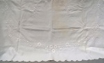 CAMA E MESA, uma (01) toalha de mesa confeccionada em linho na tonalidade branca ornada com crivos, bordado floral em linha branca, medindo 150 x 135cm aproximadamente; usada com manchas e defeitos na borda.