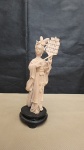 Estatueta em marfinite, representando figura de mulher tocando instrumento. Mede 18 cm de altura
