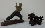 Duas esculturas sendo uma em cerâmica, representando lutador oriental com bicados na mão direita, em posição de defesa tom marrom, e outra representando dragão chines em resina no tom vermelho. Med. 15x16cm e 8x11cm