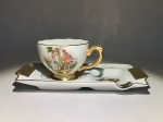 PORCELANA NACIONAL - Inusitado conjunto de xícara para café com suporte em forma de pequena travessa com divisão para cinzeiro. Detalhes a ouro e inscrição: 1o Centenário de Três Pontas. Decoração com cenas galantes. Marca de manufatura no fundo da xícara e da travessa. Medida total. 15 cm.