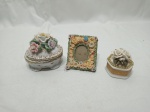 Lote de 2 pequenas caixas e 1 porta retrato, decorados com flores, sendo as caixas em porcelana e porta retrato em resina. Medindo a caixa maior 8,5cm x 6,5cm x 8cm de altura. Leves bicados.