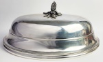 MAGNIFICA CLOCHE DE GRANDE DIMENSÃO  EM METAL ESPESSURADO A PRATA . REQUINTADA DECOIRAÇÃO COM PEROLADOS E PEGA COM FRUTO E RAMAGENS. FRANÇA, EXCEPCIONAL ESTADO DE CONSERVAÇÃO PARECENDO PRATA DE LEI. FRANÇA, INICIO DO SEC. XX. 46 X 26 CMNOTA: Uma cloche é um abafador que mantém os alimentos aquecidos até a hora do serviço. Entretanto ela confere ares de rqquinte e transmite uma sensação de opulência ao ser erguida na mesa junto aos comensais. o design do cloche  foi inspirado pelos etruscos. Graças aos desenhos deixados por esse povo, sabemos que os etruscos são conhecidos por terem criado o primeiro forno térmico conhecido. Os etruscos colocavam a massa do pão em pedras ao sol e então cobriam esta massa com um sino de cerâmica que eles frequentemente carregavam consigo. As pedras que eles escolhiam para sua massa estavam expostas ao sol e o calor que elas continham, além do calor do próprio sino (cloche) de ceramica, irradiava e assava o pão. No período gerorgiano as cloches de metal conquistaram a mesa da realeza e de seus nobres passando a ostententar brasões e a arrancar exclamações surpresas dos convidados