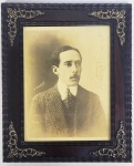 ALBERTO SANTOS DUMONT - O PAI DA AVIAÇÃO  RETRATO DE HENRY MANUEL POR VOLTA DE 1910 (HENRY MANUEL FOI FOTOGRAFO OFICIAL DO GOVERNO FRANCÊS). BELA FOTOGRAFIA COM MOLDURA EM JACARANDÁ DECORADA COM TREMIDOS E APLICAÇÃO EM METAL. APRESENTA SANTOS DUMONT POR VOLTA DO ANO DE 1910. INICIO DO SEC. XX.  31 X 25 CM COM A MOLDURA.SOMENTE A FOTOGRAFIA 23 X 17 CMNOTA: segundo relatos de um familiar ALBERTO SANTOS DUMONT Era uma figura que, à primeira vista, revelava marcada personalidade, a inspirar curiosidade e simpatia. Não fumava, só bebia nas refeições e detestava todo tipo de jogo por considerar "dissolvente do caráter dos homens". Preocupado com sua aparência era um cavalheiro. Quando criança,  conta-se que certa feita o menino Alberto brincava com seus amigos de um jogo chamado  Passarinho voa?. Era um jogo frequente entre crianças até meados do sec. Passado. Numa roda de amigos, alguém pergunta: Passarinho voa?, e todos respondem: Sim!. E o jogo continua: Abelha voa?, Galinha voa?, e assim por diante. Lá pelas tantas, para confundir, alguém indaga: Cachorro voa?. Se alguém erra a resposta, paga uma prenda. Certo dia, ao ouvir Homem voa?, Santos Dumont cravou: Sim!, para espanto de todos. Logo, sob protestos e vaias, quiseram que ele oferecesse a palma da mão em sacrifício para levar uns tapas dos amigos. Diante da zombaria do grupo, provocou: Nunca leram Júlio Verne?, quis saber o leitor precoce de clássicos da literatura universal, como Cinco Semanas num Balão, Viagem ao Centro da Terra e Vinte Mil Léguas Submarinas. E assim cresceu para dar asas materiais a sua etéria imaginação. Quando completou 18 anos, o futuro pai da aviação trocou São Paulo por Paris. Precocemente emancipado legalmente por seu pai, ajudado pelos vultosos recursos da casa paterna advindos da riqueza do rei do café no Brasil pode prosseguir rumo aos seus sonhos.  Na capital francesa, sonhava voar como os pássaros. Para realizar seu sonho, estudou, entre outras disciplinas, física, eletricidade e mecânica, e construiu, em pouco mais de dez anos, 22 máquinas voadoras, como balões, dirigíveis e aeroplanos. Em 1898, ele deu asas à primeira de suas invenções: Brasil, um balão inflado a hidrogênio, feito de seda japonesa e com seis metros de diâmetro. No dia 4 de julho de 1898, até ganhou altitude, mas não voou. Motivo: falta de vento. Seu segundo balão, batizado de América, já podia transportar alguns passageiros. Ganhou o primeiro lugar em uma competição do Aeroclube da França. Ao contrário do modelo anterior, permaneceu no ar por quase 24 horas. Até a virada do século 20, o balonismo era o único meio de transporte aéreo que existia. O problema é que, dentro de um balão,  só se pode controlar a altitude.  Santos Dumont foi o primeiro homem a conseguir voar em qualquer direção, sem ficar à mercê dos ventos. Aos 28 anos, ele conseguiu realizar um dos desejos mais antigos da humanidade. Ainda em 1898, Santos Dumont construiu seu primeiro dirigível  modelo que, como o nome já diz, pode ser dirigido ou controlado. Caiu no segundo voo. Não desistiu e deu vida ao dirigível nº 2. Caiu na primeira tentativa. No ano seguinte, criou o de nº 3. A cada novo invento, dava um número diferente. E realizava pequenos ajustes. À época, cansado de encher o balão de hidrogênio toda vez que precisava testar seu dirigível, criou o primeiro hangar  mais do que um galpão para abrigar suas geringonças infladas, o local funcionava como oficina mecânica. Com o dirigível de nº 5, chegou a contornar a Torre Eiffel, mas, no dia 8 de agosto de 1901, se chocou contra o Hotel Trocadero e ficou dependurado em seu cesto de vime a 20 metros de altura. Foi salvo pelos bombeiros. Com o dirigível de nº 6, tentou atravessar o Mediterrâneo, mas não conseguiu. Por pouco, não morreu afogado. Ao longo de sua carreira, Santos Dumont sofreu incontáveis acidentes. O importante é que ele sabia como cair. Tinha uma agilidade incrível e quase não se machucava. Na pior das hipóteses, ficava atordoado e nada mais. No dia 19 de outubro de 1901, realizou sua primeira façanha: decolou de Saint Cloud, nos arredores de Paris, deu a volta na Torre Eiffel (ou seja, contra e a favor do vento) e retornou ao ponto de partida em menos de 30 minutos. Conquistou o Prêmio Deutsch e recebeu 100 mil francos. Como não precisava do dinheiro doou o prêmio aos mecânicos de sua oficina e aos pobres de Paris. Recebeu telegrama de congratulações de outro gênio inventivo: o norte-americano Thomas Edison (1847-1931). Bandeirante dos ares!, elogiou o pai da lâmpada elétrica. E de Pedro, um amigo de infância: Você se lembra, caro Alberto, do tempo em que brincávamos de Passarinho voa?. Você tinha razão em levantar o dedo, pois acaba de demonstrá-lo voando por cima da torre Eiffel. Quando não estava em seu hangar construindo novas aeronaves ou consertando as antigas, Santos Dumont gostava de se aventurar em voos noturnos, descer no meio de uma corrida de cavalos ou, então, deixar uma mulher, Aída de Acosta (1884-1962), pilotar, sozinha, seu dirigível. Em 1903, durante o aniversário da Queda da Bastilha, sobrevoou um desfile militar em plena Champs-Élysées. Se Paris era a capital do mundo, Santos Dumont era o homem mais famoso do mundo. Naquele ano, criou o dirigível de nº 9, que ganhou o apelido de Baladeuse. Seu volante foi construído com roda de bicicleta. Pequeno e fácil de manobrar, Santos Dumont usava o primeiro carro aéreo do mundo para passear. Santos Dumont tinha mesa reservada em qualquer restaurante de Paris. Amarrava o balão a uma árvore, descia por uma escada de corda e, terminado o jantar, voltava para casa. A cidade parava para vê-lo passar. Era um playboy sui generis. Os inventos seguintes, de nº 10, 11 e 12, podem ser considerados protótipos de ônibus-voador (com capacidade para dez passageiros), hidroavião e helicóptero, respectivamente. O de nº 13, construído em 1905, foi destruído durante uma tempestade. Entre uma invenção e outra, Santos Dumont escreveu, em francês, o primeiro volume de sua autobiografia, Dans Lair (1904)  lançado no Brasil sob o título de Os Meus Balões (1938). Quatorze anos depois, publicou o segundo volume, O Que Eu Vi, O Que Nós Veremos (1918). Segundo ocupante da cadeira de número 38 da Academia Brasileira de Letras (ABL), Santos Dumont foi eleito imortal em 4 de junho de 1931, para ocupar o lugar de Graça Aranha, mas não chegou a tomar posse. Do outro lado do Atlântico, os irmãos Wilbur (1867-1912) e Orville Wright (1871-1948) também quebravam a cabeça para construir uma aeronave mais pesada que o ar. No dia 17 de dezembro de 1903, os dois levantaram voo, a bordo do aeroplano Flyer, na praia de Kitty Hawk, na Carolina do Norte. Quando os Wright convocaram a imprensa para provar que o aparelho deles voava, só conseguiram levantar voo com ajuda de uma catapulta,. É como se colocasse uma pedra em um bodoque, puxasse o elástico e a jogasse longe. Em 1906, Santos Dumont voltou a escrever seu nome na história da aviação ao criar o 14-Bis. Ao contrário dos modelos anteriores, o mais recente não era um dirigível, mas um aeroplano do tipo canard (pato, em francês), que tem o leme na parte da frente e as asas maiores na parte de trás. Para construir a aeronave, em pouco mais de um mês, usou papel de seda, hastes de bambu, pedaços de madeira e algumas peças de metal, como um motor de lancha. O 14-Bis tinha 10 metros de comprimento, 4,81 de altura e 11,5 de envergadura. E pesava 240 quilos. Os franceses apelidaram-no de Oiseau de proie (Ave de rapina). Com sua mais nova invenção, Santos Dumont fez dois voos memoráveis: no dia 23 de outubro, quando, a três metros do chão, percorreu 60 metros em sete segundos, e no dia 12 de novembro, quando, a seis metros de altura, percorreu uma distância três vezes maior, de 220 metros, ambos no Campo de Bagatelle, em Paris. Entre os milhares de curiosos que assistiram ao voo do dia 12, membros da Federação Aeronáutica Internacional (FAI). É, portanto, o primeiro voo registrado e reconhecido da história da aviação.Santos Dumont não parou ali. Até 1909, construiu mais oito modelos. Aos quatro últimos, deu o nome de Demoiselle (donzela), o primeiro ultraleve da história. O sucessor do 14-Bis chegou a alcançar a velocidade de 96 quilômetros por hora. No dia 8 de abril de 1909, percorreu 2,5 mil metros a 20 metros de altura.Santos Dumont não patenteou suas invenções. Colocou à disposição de quem quisesse reproduzi-las. Por essa razão, Demoiselle é considerada a primeira aeronave a ser fabricada em série. Foram construídos mais de 40 exemplares. Em 1910, por recomendação médica, se aposentou como piloto. Desconfia-se que sofria de esclerose múltipla. Em 1918, escolheu a cidade de Petrópolis, na serra fluminense, como residência de verão. Construiu, em apenas três meses, uma casa apelidada de Encantada. Alguns dos móveis da casa, projetada pelo arquiteto Eduardo Pederneiras, foram pensados para exercer múltiplas funções. A mesa, por exemplo. Durante o dia, era escrivaninha. À noite, virava uma cama. Os degraus das escadas são recortados no formato de raquete para facilitar a subida e evitar quedas. No banheiro, outra de suas incontáveis invenções: o chuveiro de água quente.  A mais famosa delas, com exceção do 14-Bis, é o relógio de pulso. Segundo biógrafos, teria pedido a um amigo, o joalheiro Louis Cartier (1875-1942), que fizesse um. Criou, então, um quadrado com pulseira de couro. Com o relógio de bolso, Santos Dumont não conseguia pilotar e cronometrar o tempo de voo ao mesmo tempo. Cartier, aliás, não era o único amigo famoso de Santos Dumont. Volta e meia, o piloto brasileiro saía para jantar no Maxims, seu restaurante favorito, com a princesa Isabel (1846-1921), que assinou a Lei Áurea, ou com o engenheiro Gustave Eiffel (1832-1923), que projetou a Torre Eiffel. Segundo os biógrafos de Santos Dumont, ele era baixinho  algo em torno de 1,52 metro de altura  e pesava 50 quilos. Para disfarçar sua baixa estatura, usava um chapéu panamá, terno de gola alta e sapatos de sola grossa. Tanto a fazenda Cabangu, na pequena Palmira (MG), onde nasceu, em 20 de julho de 1873, quanto a Encantada, sua residência de verão em Petrópolis, viraram museus. Hoje, sua cidade natal se chama Santos Dumont. Sobre a polêmica envolvendo a paternidade da aviação, Santos Dumont escreveu, em O Homem Mecânico: Os partidários dos irmãos Wright afirmam que foram eles que voaram na América do Norte de 1903 a 1908. Esses voos pareciam ter ocorrido perto de Dayton, num campo ao longo de uma linha de bonde. Escrito em 1929, o manuscrito O Homem Mecânico só foi descoberto 75 anos depois por um sobrinho-neto. Não posso deixar de ficar profundamente estupefato por essa reivindicação ridícula, prossegue Santos Dumont. É inexplicável que os irmãos Wright pudessem ter realizado inúmeros voos durante três anos e meio sem terem sido observados por um único jornalista da perspicaz imprensa norte-americana que tivesse se dado o trabalho de assisti-los e de produzir a melhor reportagem da época, conclui. No dia 23 de julho de 1932, Santos Dumont foi encontrado morto, enforcado com duas gravatas, no banheiro de seu quarto no Hotel de La Plage, no Guarujá (SP). Até hoje, não se sabe ao certo o que teria levado o pai da aviação a cometer suicídio. Uma das hipóteses é a de que ele teria entrado em depressão ao ver seu principal invento usado como máquina de guerra na Revolução Constitucionalista de 1932. Nunca pensei que fosse causar derramamento de sangue entre irmãos, teria dito ao ascensorista do hotel, Olympio Peres Munhoz, minutos antes de sair do elevador. O que eu fiz?. Por mais de 20 anos, acreditou-se que Santos Dumont teria morrido de um colapso cardíaco, como atestava sua certidão de óbito. Seu coração foi guardado em um pequeno cofre de ouro e no formato de esfera celeste no Museu Aeroespacial, no Campo dos Afonsos, e seu corpo sepultado no Cemitério São João Batista, em Botafogo, ambos no Rio de Janeiro. Uma curiosidade: foi o próprio Santos Dumont quem mandou erguer o jazigo, ornamentado pela estátua em bronze de Ícaro, ao lado dos pais, Henrique e Francisca. Ficou muito bonito, escreveu ao sobrinho Alberto, em 19 de outubro de 1923. Não podia ser mais a meu gosto. Entre outras homenagens, Santos Dumont virou nome de rua, praça e aeroporto. Em 1973, no centenário de seu nascimento, a União Astronômica Internacional (IAU, na sigla em inglês) deu o nome do inventor brasileiro a uma cratera lunar de 8,8 km de diâmetro, que fica próxima ao local de pouso da missão Apollo 15. (excertos do texto de ANDRÉ BERNANDO para BBC BRASIL: Santos Dumont, 150 anos: as aventuras (e desventuras) do 'pai da aviação')