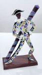 Escultura decorativa representando personagem estilizado Pierrô / Pierrot  Arlequim, em cerâmica esmaltada policromada, atribuída à Tasca. A figura apresenta postura dinâmica, apoiada em um longo bastão, com vestimenta decorada por padrão geométrico multicolorido típico do traje de arlequim. O acabamento esmaltado confere brilho e destaca as cores vivas da composição. A peça encontra-se montada sobre base retangular em tom marrom-escuro, garantindo boa estabilidade. Trata-se de um objeto decorativo expressivo, ideal para colecionadores ou para compor ambientes com um toque artístico e original.Dimensões:Aproximadamente 37 x 12 cm (altura x base).Estado de conservação:Bom estado geral.