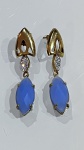 Par de brincos composto por pedras azuis em formato oval com lapidação que valoriza a transparência e o brilho das gemas. As pedras encontram-se emolduradas por estrutura metálica dourada.