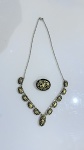 Conjunto composto por colar articulado e broche, com elementos ovais em fundo preto e decoração dourada de motivos clássicos. Colar com sequência de placas e pingente central. Estrutura metálica em tom dourado, fecho funcional.Em bom estado de conservação, com sinais compatíveis com o uso. Ideal para uso social ou coleção.