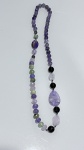 COLAR EM PEDRAS NATURAIS MULTICOLORIDAS (TONS DE LILÁS E VERDE)Colar longo composto por contas em pedras naturais, predominantemente em tonalidades de lilás, roxo e verde, com variações translúcidas e acabamento polido. As contas apresentam formatos esféricos e irregulares, intercaladas por elementos de maior dimensão, incluindo peças facetadas e lapidações diferenciadas.Destaque para elemento central em pedra de maior porte, em formato orgânico/facetado, que confere protagonismo visual à composição. Intercalações com contas em tons escuros e translúcidos agregam contraste ao conjunto.Montagem em fio contínuo, sem fecho aparente, permitindo uso versátil e bom caimento.Material: pedras naturais diversas (possivelmente quartzos e variações, não testadas).Elementos complementares: contas em material translúcido (vidro e/ou cristal).Estado de conservação: bom.