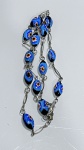 COLAR EM VIDRO MILLEFIORI AZUL COM MONTAGEM METÁLICAColar composto por contas em vidro na técnica millefiori, em formato ovalado, com predominância da cor azul e aplicação de motivos florais multicoloridos (tons de amarelo, branco, vermelho e preto) incorporados à massa vítrea.As contas apresentam acabamento polido e alto brilho, com padrão decorativo característico da técnica. Montagem articulada por elos metálicos, intercalando as contas e proporcionando mobilidade e bom caimento à peça.Fecho metálico presente, em tom prateado, compatível com o conjunto.Material: vidro millefiori.Elementos complementares: metal (elos e fecho).Estado de conservação: bom
