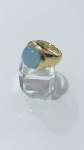 ANEL COM PEDRA EM CABOCHÃO EM TONALIDADE AZUL CLAROAnel com aro robusto em metal de tonalidade dourada, apresentando design volumoso e acabamento polido.A peça é encimada por pedra em formato cabochão oval, em tonalidade azul claro, com superfície lisa e brilho suave, conferindo destaque central ao conjunto.PERÍODO: contemporâneoMATERIAL: metal e pedra (não identificada)TÉCNICA: fundição, polimento e cravaçãoESTADO DE CONSERVAÇÃO: bom estado geral, com leves sinais de uso compatíveis. Pedra íntegra, sem lascas aparentes.OBSERVAÇÕES: anel de presença marcante, com estética elegante e contemporânea, destacando-se pelo contraste entre o metal dourado e a pedra em tom azul claro.