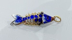 PINGENTE EM METAL DOURADO COM ESMALTAÇÃO REPRESENTANDO PEIXEPingente em metal de tonalidade dourada, modelado em forma de peixe, com rica decoração em esmaltação nas cores azul, branco e detalhes em vermelho, evidenciando escamas e elementos anatômicos estilizados.Apresenta trabalho minucioso com relevos e aplicações, conferindo textura e destaque visual à peça. Argola superior integrada para uso em correntes ou pulseiras.PERÍODO: contemporâneoMATERIAL: metal dourado e esmalteTÉCNICA: fundição, esmaltação e acabamento manualESTADO DE CONSERVAÇÃO: bom
