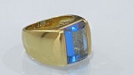 ANEL EM METAL DOURADO COM PEDRA EM FORMATO RETANGULARAnel de aro robusto em metal de tonalidade dourada, com design liso e volumoso, apresentando linhas retas e contemporâneas.A peça é encimada por pedra de formato retangular com faces planas, em tonalidade azul translúcida, proporcionando efeito de profundidade e destaque visual.PERÍODO: contemporâneoMATERIAL: metal dourado e pedra (não identificada)TÉCNICA: fundição, lapidação e montagemESTADO DE CONSERVAÇÃO: bom estado geral.
