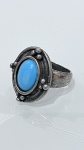 ANEL EM METAL PRATEADO COM PEDRA AZULAnel em metal prateado, com aro robusto e topo ovalado, apresentando pedra azul em lapidação cabochão. A pedra é envolvida por moldura elevada, com decoração em relevo composta por pequenos elementos esféricos, conferindo aspecto artesanal à peça.O acabamento levemente oxidado valoriza os detalhes e cria contraste com a tonalidade intensa da pedra, evidenciando o desenho orgânico do conjunto.PERÍODO: contemporâneoMATERIAL: metal prateado e pedra azulTÉCNICA: fundição, cravação tipo bisel e acabamento oxidadoESTADO DE CONSERVAÇÃO: bom estado geral, com sinais de uso compatíveis com o tempo, sem danos aparentes na pedra.