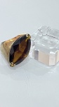 ANEL EM METAL DOURADO COM PEDRA FACETADAAnel em metal dourado, de aro robusto e design marcante, apresentando pedra de grande dimensão em lapidação facetada, em formato alongado. A pedra é fixada por garras, destacando seu brilho e profundidade de cor em tom âmbar.O conjunto possui estética imponente, com linhas simples que valorizam o volume e a presença da pedra central.PERÍODO: contemporâneoMATERIAL: metal dourado e pedra sintética ou natural de coloração âmbarTÉCNICA: fundição e cravação por garrasESTADO DE CONSERVAÇÃO: bom estado geral