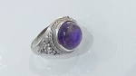 ANEL EM PRATA DE LEI COM PEDRA ROXAAnel em prata de lei, apresentando aro trabalhado com detalhes em relevo e acabamento decorativo nas laterais. O topo é composto por pedra roxa em lapidação cabochão, de formato oval, destacada por moldura elevada que valoriza sua cor e brilho.O conjunto apresenta estética marcante, com inspiração em peças artesanais, unindo robustez e riqueza de detalhes.PERÍODO: contemporâneoMATERIAL: prata de lei e pedra roxaTÉCNICA: ourivesaria, cravação tipo bisel e acabamento em relevoESTADO DE CONSERVAÇÃO: bom estado geral