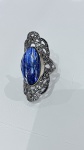 ANEL EM PRATA DE LEI COM PEDRA AZUL LAPIDADAAnel confeccionado em prata de lei, apresentando aro com rica decoração vazada e detalhes em relevo, remetendo a trabalho artesanal de inspiração clássica.O destaque da peça é sua pedra central de coloração azul intensa, em lapidação facetada, exibindo tonalidade profunda que varia entre o azul marinho e nuances levemente mais claras conforme a incidência de luz. A superfície facetada proporciona brilho sutil e reflexos elegantes, conferindo presença marcante ao conjunto.Montagem em caixa alta, valorizando a pedra e garantindo maior destaque visual. Peça de bom impacto estético, com acabamento trabalhado que agrega sofisticação e caráter ornamental.
