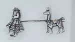 BROCHE EM PRATA COM MOTIVO FIGURATIVO  PERSONAGEM E ANIMALBroche confeccionado em prata, sem marca de teor aparente, composto por duas figuras interligadas por corrente metálica.De um lado, representação de personagem estilizado com vestimenta típica e detalhes gravados em relevo. Do outro, figura de animal, possivelmente uma lhama, com modelagem tridimensional e acabamento polido.As peças são conectadas por corrente torcionada, conferindo mobilidade ao conjunto. Fixação posterior por pinos independentes.Acabamento com áreas polidas e levemente oxidada, evidenciando os detalhes do relevo. Peça de caráter decorativo, em bom estado geral de conservação.