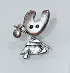 BROCHE EM PRATA DE LEI COM FIGURA ESTILIZADABroche confeccionado em prata de lei, sem marca de teor aparente, representando figura estilizada de personagem em composição lúdica.Apresenta modelagem em relevo com traços simplificados, destacando cabeça em formato arredondado com dois pontos escurecidos representando os olhos, corpo com vestimenta e elemento acessório apoiado sobre o ombro.Acabamento com áreas polidas e levemente texturizadas, conferindo contraste visual. Fixação posterior por pino.Peça de caráter decorativo, com estética moderna e expressiva, em bom estado geral de conservação.