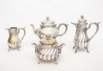 Christofle - França - Elegante conjunto para chá e café em metal espessurado a prata cerca de 1900 ricamente cinzelado com gomos, conchas e volutas, bojos monogramados apoiados sobre três pés, marca da manufatura na base constando de um bule de chá com isoladores em marfim na alça - med. 17x27x13 cm (com pequenas mossas no bojo), um bule para café, alça com isoladores em marfim - med. 25x18x8 cm (com pequeno amassado na ponta), uma  cremeira - med. 16x14x7 cm e um açucareiro com alças laterais - med. 16x18x12 cm (com pequenos amassados na borda interna da tampa e no bojo, peças com pequenos desgastes no banho de prata do uso e do tempo) - Total de 4 peças