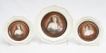 Bavária - Conjunto de três antigos pratos decorativos para parede em porcelana branca com as bordas vazadas, medalhões centrais decorados com figuras femininas policromadas, marca da manufatura na base, dois pratos de sobremesa - med. 19,5 cm de diâmetro e um prato raso - med. 25 cm de diâmetro