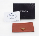 Prada - Milano - Porta cartões de couro Saffiano no tom castanho, com logo triangular esmaltado, compartimentos para cartões med. 10,5x7 cm (com pequenas manchas de guardado no verso), acondicionado em caixa original, acompanha certificado de autenticidade.