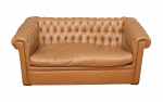 Elegante sofá Chesterfield estilo Inglês para dois lugares em couro no tom caramelo, encosto e braços em capitonê, assento solto med. 73x165x87 cm (com pequeno rasgo da almofada do assento, um arranhão na lateral de um braço e dois botões faltando acabamento).