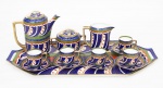 Antigo e elegante conjunto para café cerca de 1930 em porcelana da Checoslováquia ricamente policromado, decorado com folhagens e realces a folha de ouro sobre fundo nas cores azul cobalto, verde, coral e branco, constado de um bule de café med. 17x16x9 cm, uma cremeira med. 11x12x7 cm, um açucareiro med. 9x13x9 cm, cinco xícaras de café com pires e uma bandeja com alças laterais med. 53x27 cm. Total de 9 peças, marca da manufatura na base.