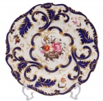 Porcelana - Belíssimo prato de coleção com decoração em azul e ouro sobre fundo branco - tema floral no centro, sem marca de manufatura aparente. Europa - Século XIX. 2 x 22,5 cm (ME). Marcas e desgastes do tempo. Acervo Particular Rio de Janeiro/RJ.