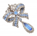 Joia - Antigo e belíssimo broche de estilo antigo, na forma de laço guarnecido por pingente. Estrutura de prata contrastada, cravejada por pedras nas cor azul de diversas lapidações e marcassitas. Med. 5 x 3,5 cm(ME). Peso total: 14,1 gramas . Marcas do tempo e de uso. Acervo Particular Rio de Janeiro/RJ.