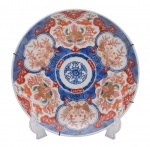 Arte Oriental - Belíssimo prato de porcelana japonesa dita "imari", profusamente decorado, em sua policromia característica, pelos esmaltes nas cores azul índigo, vermelho e "rouge de fer" sobre fundo branco, reproduzindo as temáticas floral e grafismos. Japão -Séc. XX. Med. 32cm (ME). Marcas do tempo. Acervo Particular Rio de Janeiro/RJ.