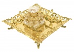 Belíssimo tinteiro de bronze dourado de estilo império, formato quadrado. Quatro pés. Galeria vazada. suporte para pena, Recipiente para tinta de cristal europeu lapidado. Presença de inscrições. Med. 13 x 23 x 23 cm (medidas totais). 8 x 7 x 7 cm (recipiente para tinta). Marcas do tempo. Acervo Particular Rio de Janeiro/RJ.