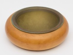 VIDE POCHE em madeira clara de formato circular e contorno abaulado, centralizando prato em metal liso. OBS: (Oxidação no metal). Med. Alt. 8,0 cm  Diâm. 27,0 cm.