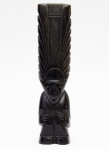 ESTATUETA em onix preto, possivelmente mexicana, representando figura estilizada de divindade. Apresenta-se em postura reta encimada por grande adorno de cabelo. Med. Alt. 25,5 cm.