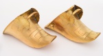 PAR DE ANTIGAS Sapatas espanholas para criança em metal dourado com argolas de sustentação ladeadas por concheados. Frentes ornadas por fivelas retangulares aplicadas em relevo. Peças de coleção com rara decoração. Século XIX. OBS: (defeitos do tempo na lateral de uma e na sola do outra). Med. Compr. 20,0 cm