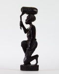 ESCULTURA AFRICANA em madeira representando caçador meio ajoelhado com presa sobre a cabeça e apoiado sobre pequena base entalhada. Med. Alt. 33 cm.