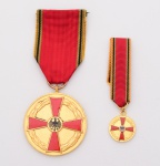 CONJUNTO de Medalha de Mérito da República Federal daAlemanha e miniatura de lapela. Anverso com cruz de Malta centralizandopequeno medalhão com águia. Reverso com a inscrição Fur Verdienste um dieBundesrepublik Deutschland, i.e. Para serviços prestados para a RepúblicaFederal da Alemanha. Metal dourado.com esmaltes vermelhos e pretos. Acompanham fitilhos originais. Década de1950-1960.  Med. Diâm. 4,0 cm e  1,5 cm.