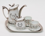 PORCELANA SCHMIDT  Serviço comemorativo, "bodas de prata", Tête à tête em porcelana brasileira branca, ornada com filetes eadornos em esmaltes. Apresentam, dentro de coroas de louros, os dizeres Bodas de Prata e os números 25 no verso. Bojos noformato de balaústres cônicos, com bicos recurvos, alças laterais em S e tampas com pegas estilizadas. Bases realçadas por faixas com estilizações florais. Constando de bule com pequeno descanso acoplado à bandeja (Med. Alt. 27,0 cm X 16,0 cm), açucareiro (Med. Alt. 11,0 cm), e 2 xícaras (Med. Alt.5,0 cm) com seus 2 pires (Med. Diâm. 9,0 cm).Total : 7 peças. Marcas da manufatura de Santa Catarina sob as bases.