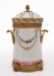 CAIXA CILINDRICA em porcelana com fina rede de craquelê, decorada em esmaltes policromados. Apresenta ornamentação em bronze dourado com bordas, alças no formato de folhas e base geometrizada com pés revirados. Bojo reto, ornado por guirlandas e friso inferior com flores. Tampa no estilo encimada por pega em pinha. Sob a base marca deItalianism Porcelain. Med. Alt. 31,0 cm   Diâm. 16,0 cm.