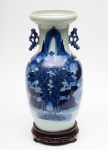 VASO em porcelana chinesa azul e branco, decorado com paisagem montanhosa, vegetações e pagodes. Possui duas alças com formato de dragões estilizados. Acompanha pedestal em madeira ebanizada. Sem Marca na base.  Med. Alt. 43,0 cm  Larg. 22,0 cm