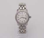 BAUME & MERCIER -  Relógio de pulso em aço com caixa circular lisa. Mostrador branco com algarismos árabes e dia do mês. Pulseira montada em elos com fecho dobrável e invisível. Numeração: MOA08632  3806923. Acompanham caixa original e manual. OBS: Funcionando. Med. Diâm. 3,5 cm.